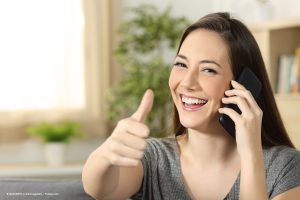 Frau mit langen Haaren lacht in die Kamera. Sie hält ein Handy am Ohr und den rechten Daumen hoch. Christine Kiunke KIUNKE Coaching zum WIR