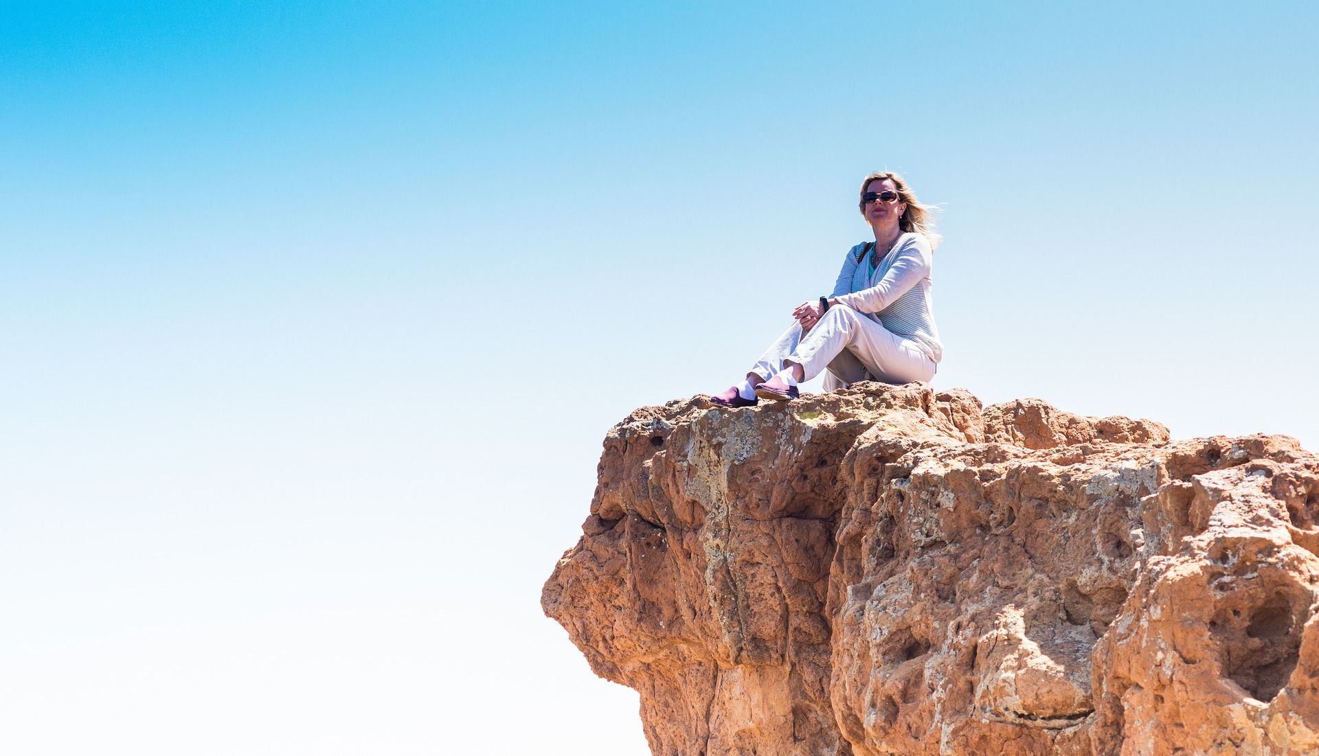 Frau sitzt zufrieden auf einem zerklüfteten Fels. Über ihr blauer Himmel. Sie hat bildlich einen Berg von Aufgaben bewältigt. Christine Kiunke Coaching für Frauen mit Firma und Familie