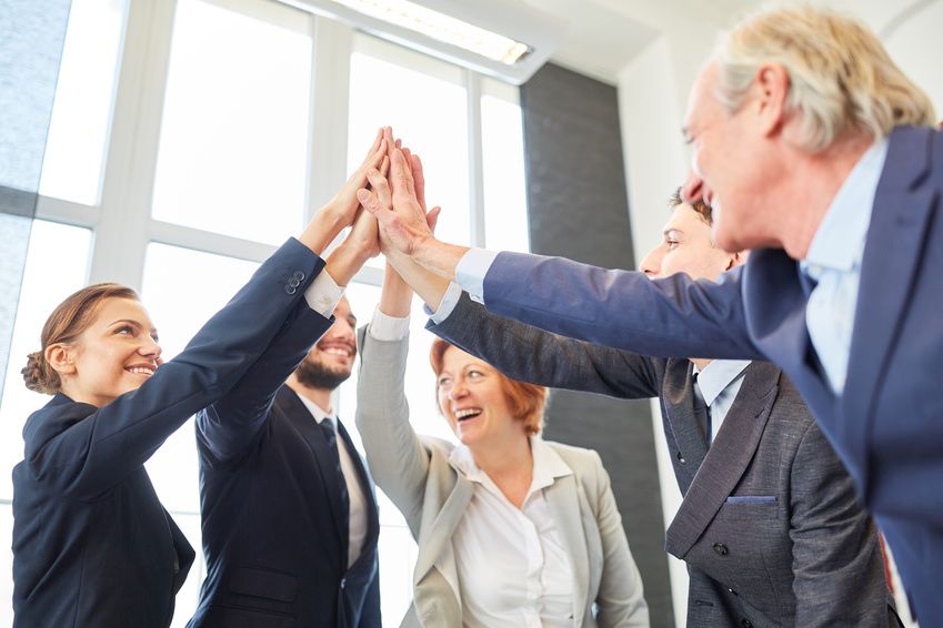 Fünf Mitarbeiter*innen strecken die Hände zu einem High Five. Erfolgreiche Zusammenarbeit durch einen Team-Workshop mit Christine Kiunke